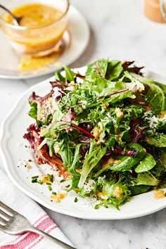 a white plate topped with a salad next to a fork and glass of orange juice