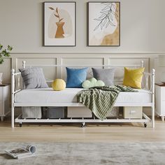 a white daybed with pillows and blankets on it in a room next to two framed pictures