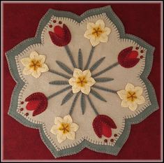 a white doily with red and yellow flowers on the center is hanging on a red wall