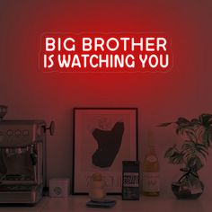 a neon sign that says big brother is watching you on the wall next to a coffee maker