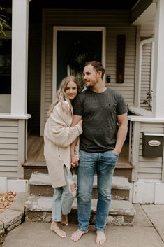 a man and woman standing on the front steps of a house with their arms around each other