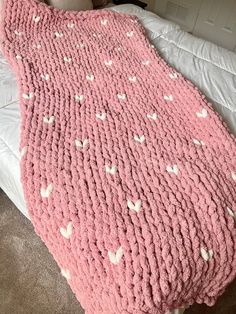 a pink crocheted blanket with white hearts on it sitting on top of a bed