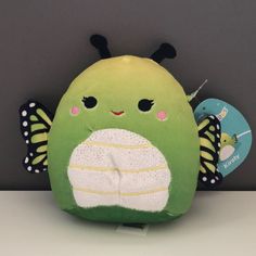 a green stuffed animal sitting on top of a white table next to a gray wall