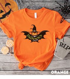 "Get ready to spread your wings and embrace the spooky spirit with our \"Halloween Party\" t-shirt! Whether you're planning to attend a Halloween party, go trick-or-treating, or just want to showcase your love for the season, this t-shirt is the perfect choice. 🦇 Unique Bat Design: Our eye-catching bat design adds a touch of mystery to your Halloween attire. The intricately detailed bat graphics give a nod to the night's spooky inhabitants while maintaining a fun and approachable vibe. 🦇 Versatile and Festive: This t-shirt is a versatile addition to your Halloween wardrobe. Wear it with jeans, leggings, or even as a part of a creative costume ensemble. It's a great way to express your love for Halloween without going over the top. Embrace the magic and spookiness of Halloween with this c Halloween Themed Short Sleeve Shirt, Themed Halloween Short Sleeve Shirt, Orange Halloween T-shirt With Letter Print, Halloween Orange Crew Neck T-shirt, Orange Letter Print Shirt For Halloween, Orange Graphic Print Shirt For Halloween, Halloween Orange Graphic Print T-shirt, Orange Halloween Graphic T-shirt, Orange Crew Neck Shirt For Halloween