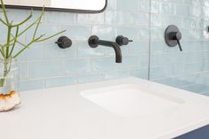 a bathroom sink with two faucets and a vase filled with flowers on the counter