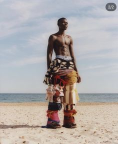 a man standing on top of a sandy beach next to the ocean with his legs crossed