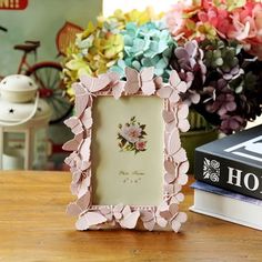 there is a pink flower frame on the table next to some books and vases