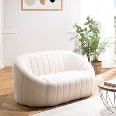 a white couch sitting on top of a hard wood floor next to a potted plant