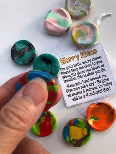 a person pointing at some colorful marbles on a white table with a sign that says worry stone