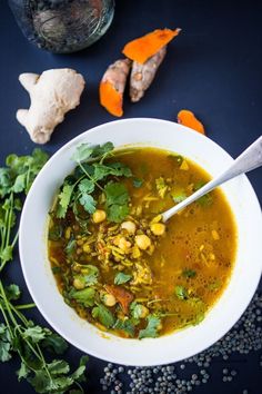 a white bowl filled with soup next to carrots and parsley on a blue surface