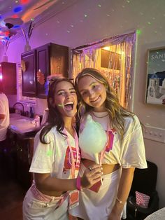 two young women standing next to each other in a room with lights on the ceiling