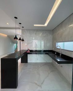 an empty kitchen with marble counter tops and black counters, along with pendant lights hanging from the ceiling