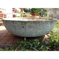 a large stone bowl sitting on top of a brick floor next to grass and bushes