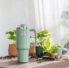 a green coffee cup sitting on top of a wooden table next to potted plants