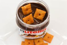 some crackers are sitting in a jar on a white plate next to chocolate sauce