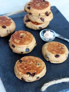 four pancakes with blueberries and butter on a black slate board next to a spoon