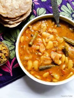 a bowl of soup and some pita bread on a colorful table cloth with a spoon