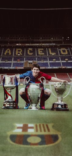 a man kneeling down next to two trophies on top of a soccer field in front of an empty stadium