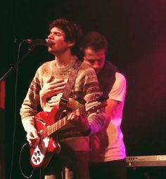 two young men standing next to each other while playing guitars and singing into microphones