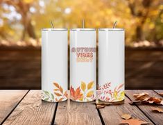 three stainless steel tumblers with autumn vibes on them sitting on a wooden table