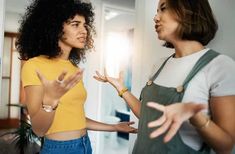 two women are talking and having fun in the living room with their hands out to each other