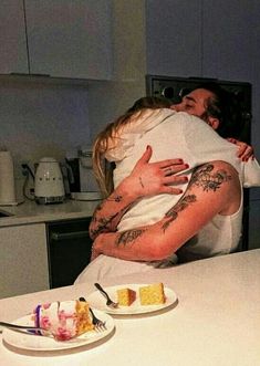 a woman hugging her husband in the kitchen with cake on the counter and two plates