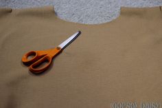 a pair of scissors sitting on top of a piece of brown fabric next to a hole in the cloth