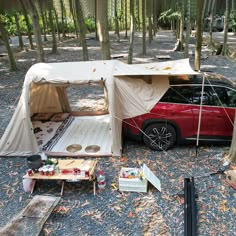 a red car is parked in the woods next to a tent and picnic table with food on it