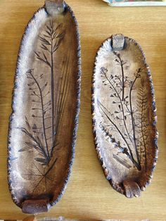 two metal spoons with designs on them sitting on a wooden table next to each other