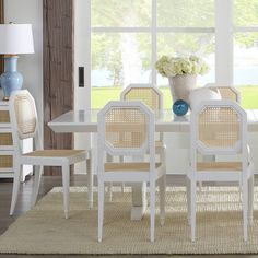 a white table and chairs in front of a large window with flowers on the table