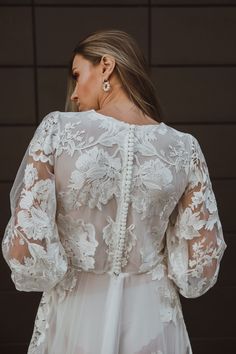 the back of a woman wearing a white wedding dress with long sleeves and pearls on it