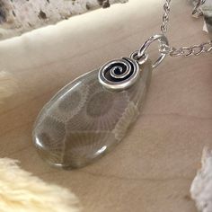 Embrace the natural beauty of Michigan with this Handcrafted Petoskey Stone Cabochon Pendant. This stunning piece features a beautifully polished Petoskey stone, skillfully shaped into a cabochon and adorned with a drilled hole for versatility. Attached to a durable stainless steel jump ring, this pendant is embellished with a charming swirl charm, adding a touch of whimsy and elegance to the design. Measuring approximately 0.75 x 1.2 inches, each stone is uniquely crafted, showcasing the distin Nickel-free Sterling Silver Swirl Necklace, Sterling Silver Swirl Jewelry Gift, Adjustable Spiral Necklace Nickel Free, Sterling Silver Swirl Jewelry As A Gift, Silver Swirl Necklace For Gifting, Adjustable Spiral Nickel-free Necklace, Silver Swirl Necklace For Gift, Silver Swirl Necklace Perfect For Gifts, Silver Swirl Jewelry For Gift