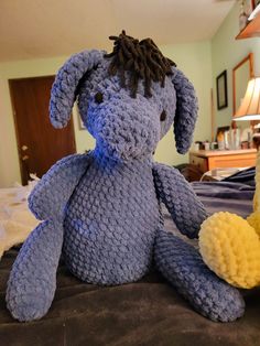 a blue stuffed animal sitting on top of a bed next to a yellow stuffed animal