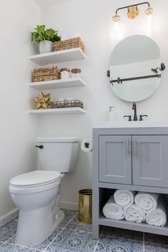 a white toilet sitting next to a bathroom sink under a mirror and shelves filled with towels