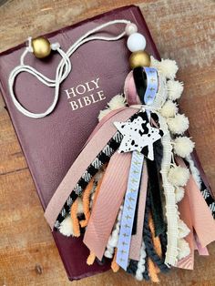 an open bible on a wooden table with ribbon and beads attached to the front cover