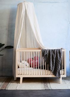 a baby crib with a white canopy over it's head in front of a blue wall