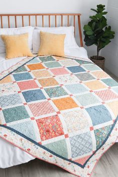 a bed with a quilt on top of it next to a potted green plant