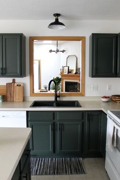 a kitchen with dark green cabinets and white counter tops is seen in the mirror above the sink