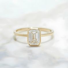 an emerald - cut diamond ring sits on a marble surface in front of a white background