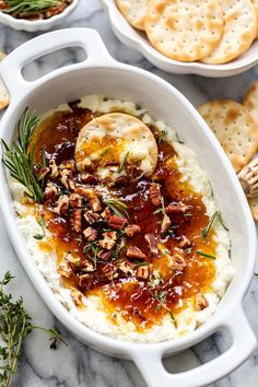 mashed potatoes in a white casserole dish with rosemary garnish and crackers