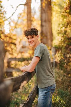 a young man leaning on a fence in the woods