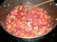 a pot filled with lots of vegetables cooking on top of a stove next to a wooden spoon