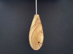 a wooden object hanging from a string on a black wall with a white light behind it