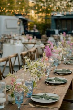 a long wooden table with plates and glasses on it is set for an outdoor dinner