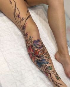 a woman's leg with flowers and vines tattooed on her legs, sitting on a bed