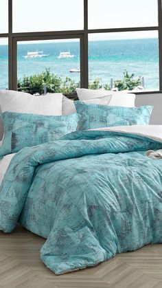 a bed with blue comforter and pillows in front of a window overlooking the ocean