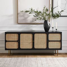 a black and gold sideboard with two vases on it in front of a white wall