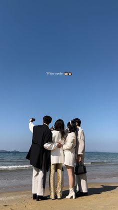 four people standing on the beach looking at an airplane in the sky