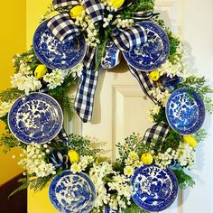 a wreath with blue and white plates hanging on it's front door decorated with yellow flowers