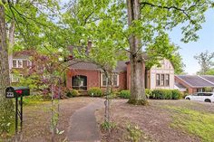 a brick house surrounded by trees in the middle of a yard with a mailbox